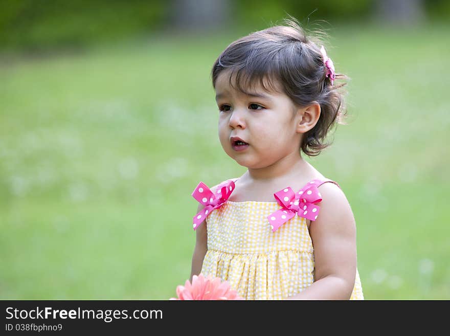 Beautiful little brunette girl outdoors with a questioning expression on her face and wearing a yellow sundress with pink dotted bows. Beautiful little brunette girl outdoors with a questioning expression on her face and wearing a yellow sundress with pink dotted bows