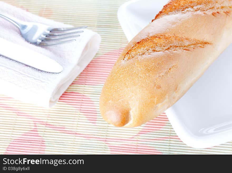 Baguette on white plate, napkin, fork and knife