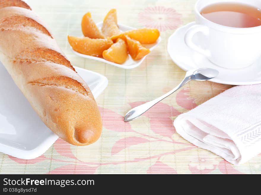 Crisp fresh-baked baguette on white plate, peach dessert and a cup of tea on bamboo placemat. Crisp fresh-baked baguette on white plate, peach dessert and a cup of tea on bamboo placemat