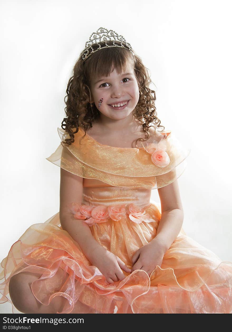 The girl the princess in a orange dress sits opposite to a white background. The girl the princess in a orange dress sits opposite to a white background