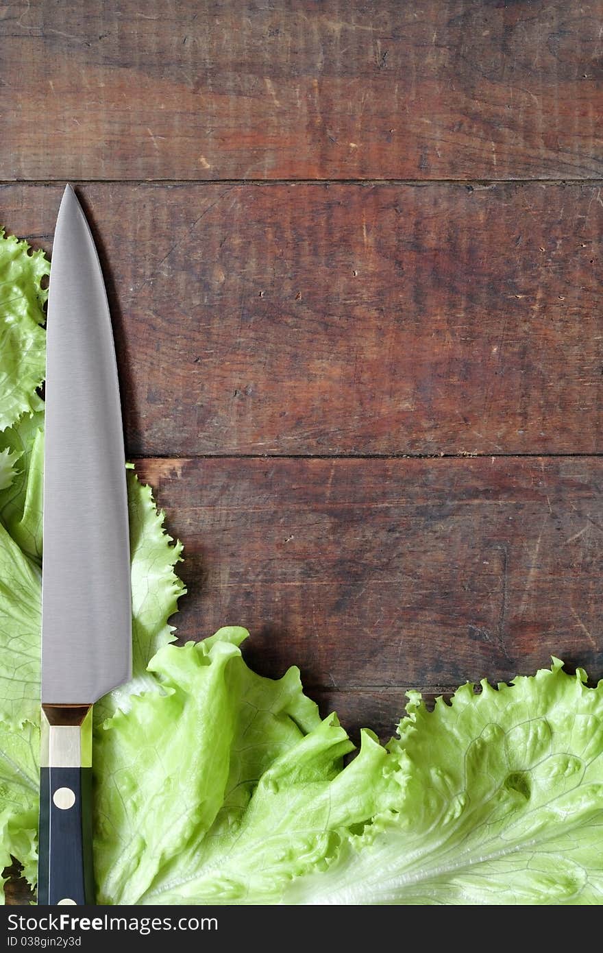 Kitchen knife and green leaves of lettuce lying on wooden surface with copy space. Kitchen knife and green leaves of lettuce lying on wooden surface with copy space