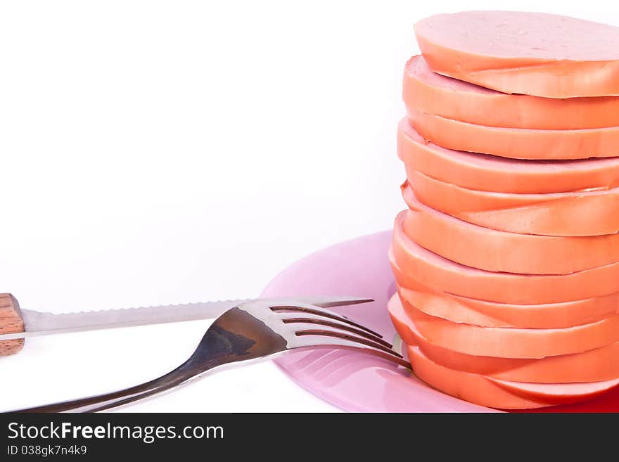 Cooked sausage on the plate with knife and fork across white. Cooked sausage on the plate with knife and fork across white