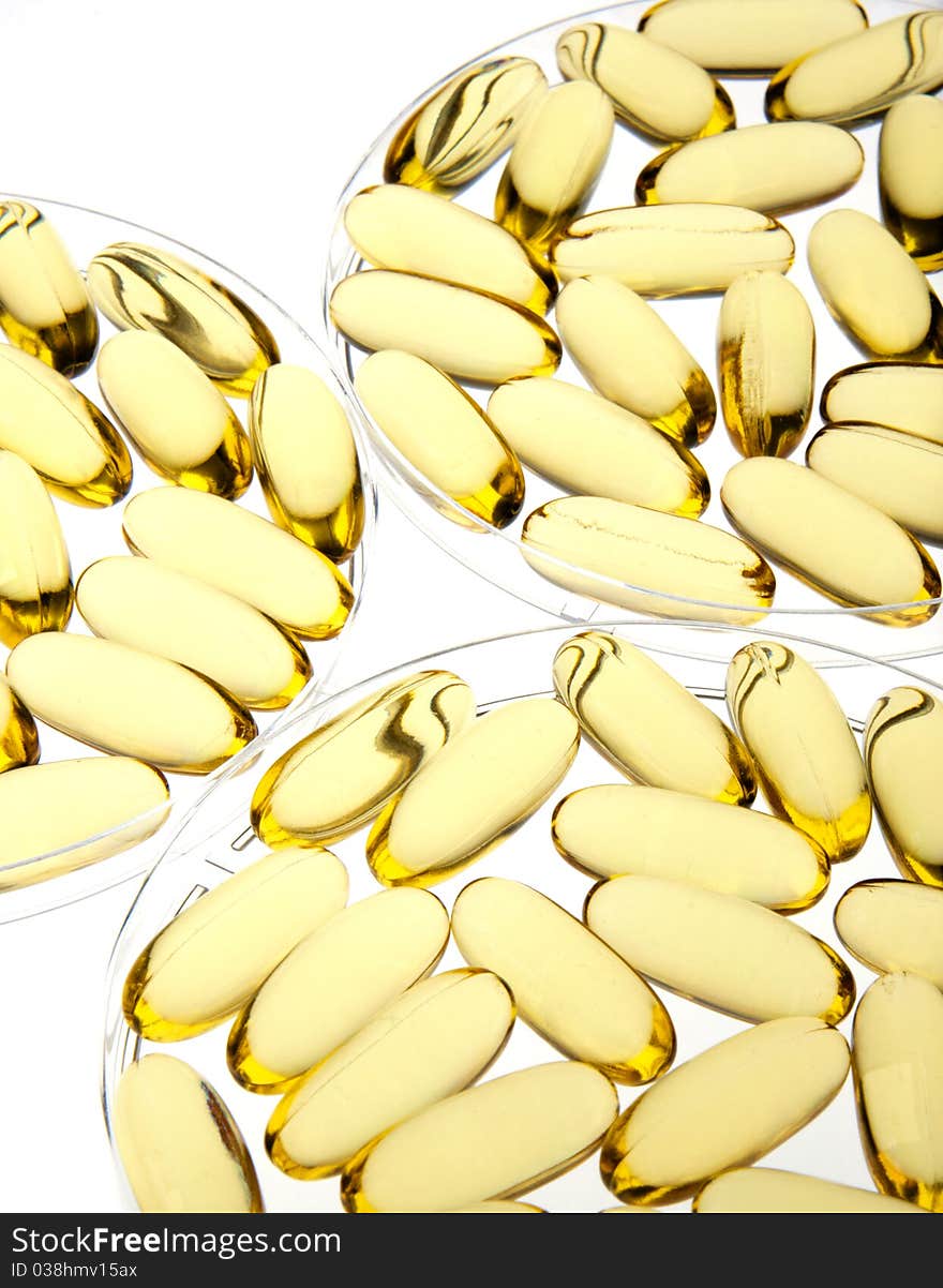 Gold pills or capsules backlit on white for medical or science use in petri dishes. Gold pills or capsules backlit on white for medical or science use in petri dishes