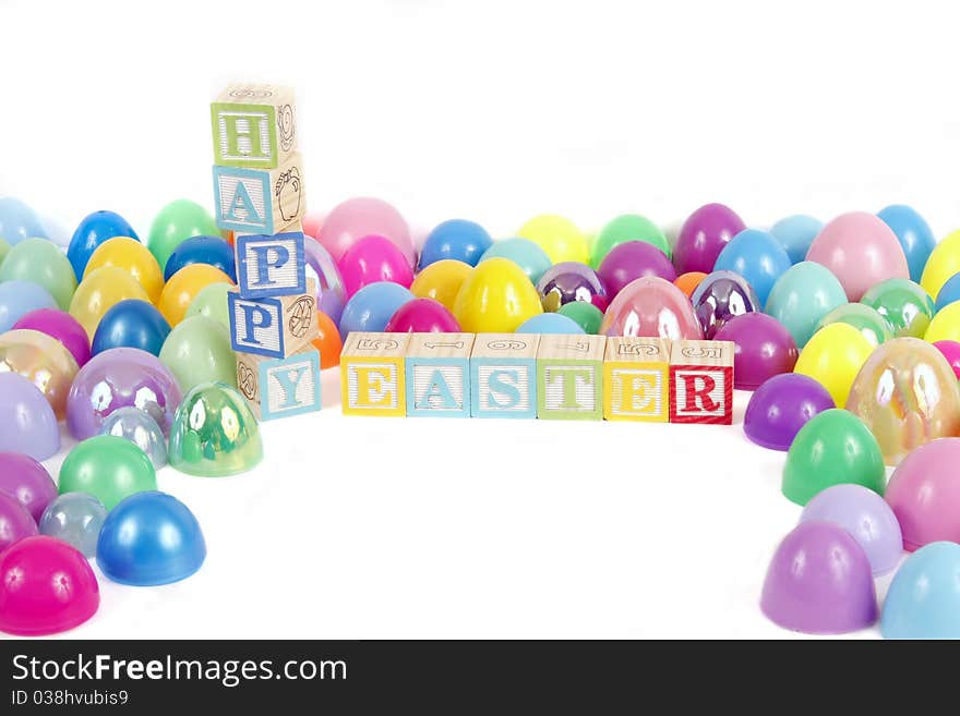 Childrens blocks spell Happy Easter with colorful plastic eggs on a white background.