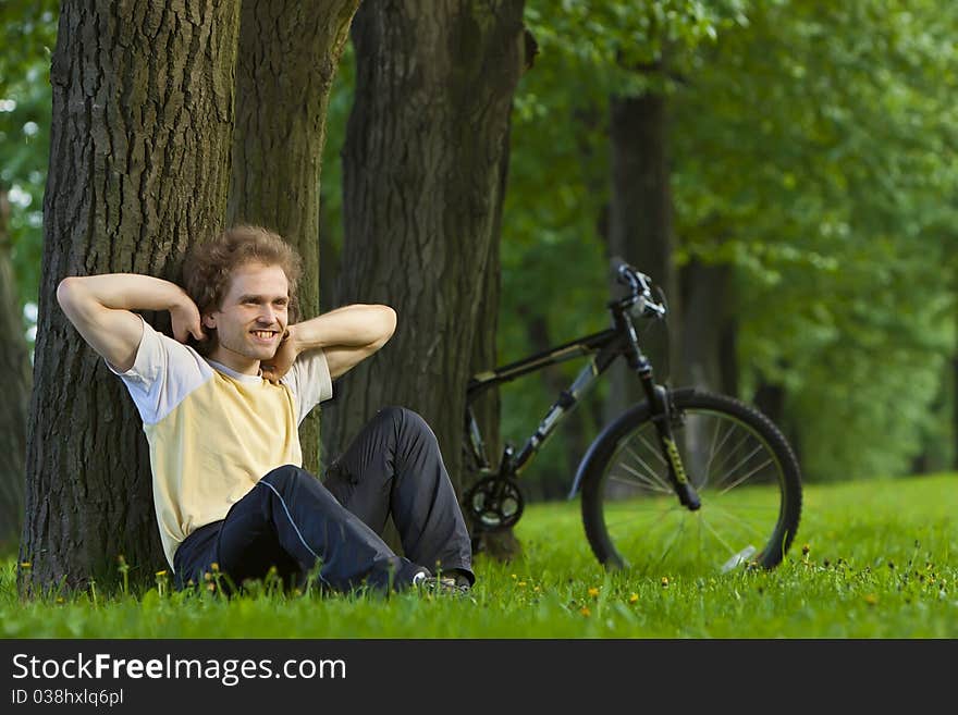 Young man siting under the tree near his bycicle