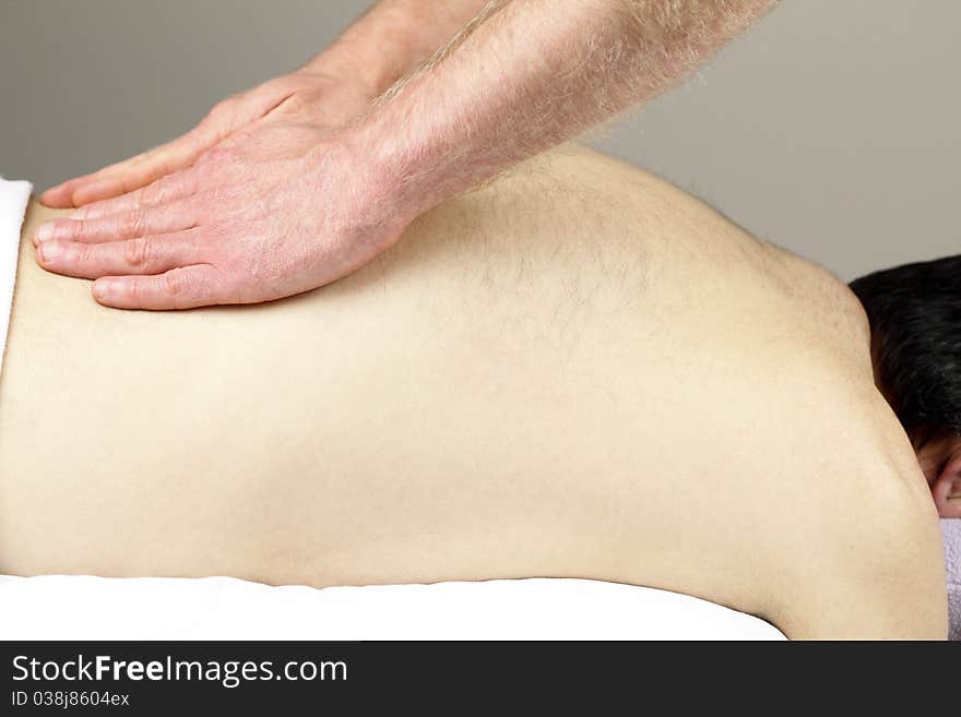 Mature male who is face down on a massage table is having his low back massaged by a masseur. Mature male who is face down on a massage table is having his low back massaged by a masseur.