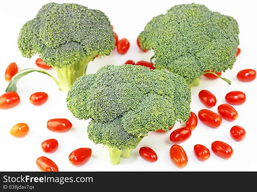Three crowns of green vegetable standing upright with many small red fruit on white. Three crowns of green vegetable standing upright with many small red fruit on white.
