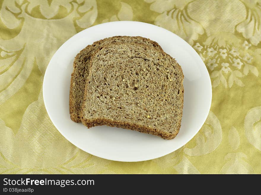 Two crisp whole sprouted grain and legume bread slices on a round white dish above a buttery yellow floral cloth placemat. Two crisp whole sprouted grain and legume bread slices on a round white dish above a buttery yellow floral cloth placemat.