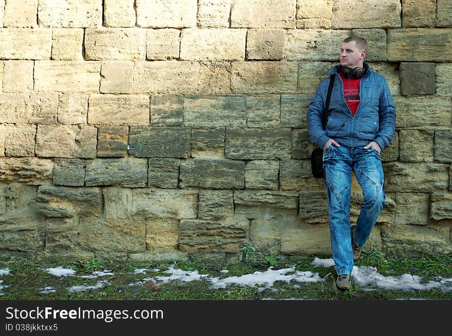 The guy with earphones stand near a brick wall. The guy with earphones stand near a brick wall