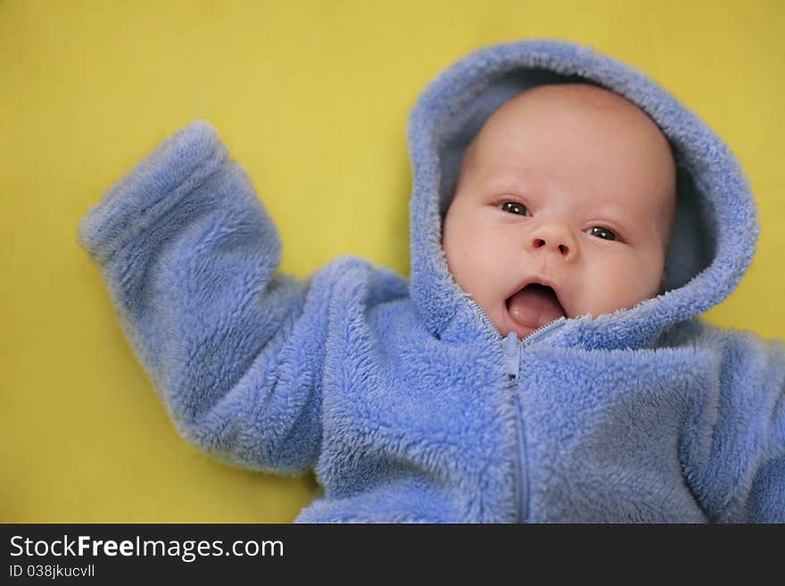 The cheerful baby in blue overalls on a yellow background (Small depth of sharpness). The cheerful baby in blue overalls on a yellow background (Small depth of sharpness)