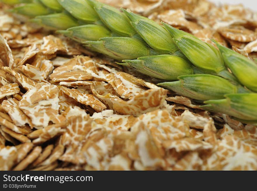 A pile of wheat flakes with a green ear of wheat close-up. A pile of wheat flakes with a green ear of wheat close-up