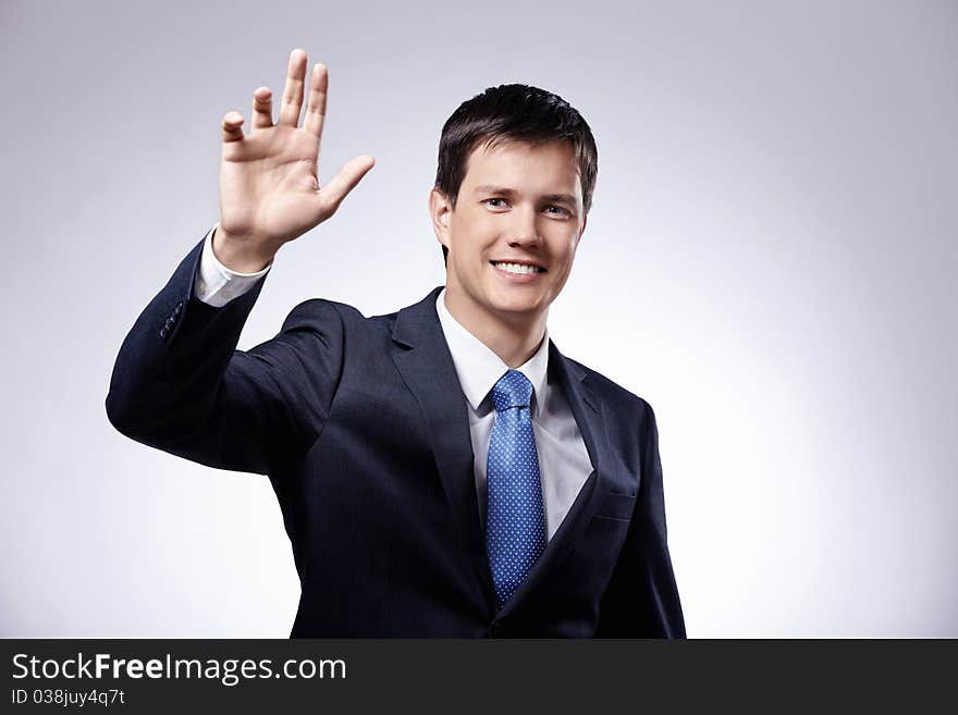 Attractive man in a suit with his hand raised on a gray background. Attractive man in a suit with his hand raised on a gray background