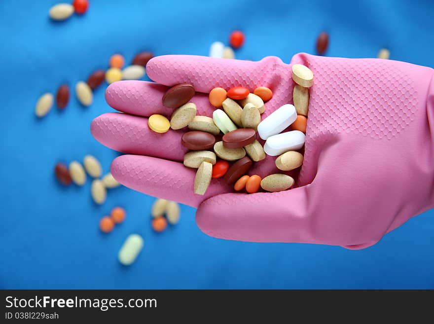 A group of various pills sit pink gloves and blue background. A group of various pills sit pink gloves and blue background.