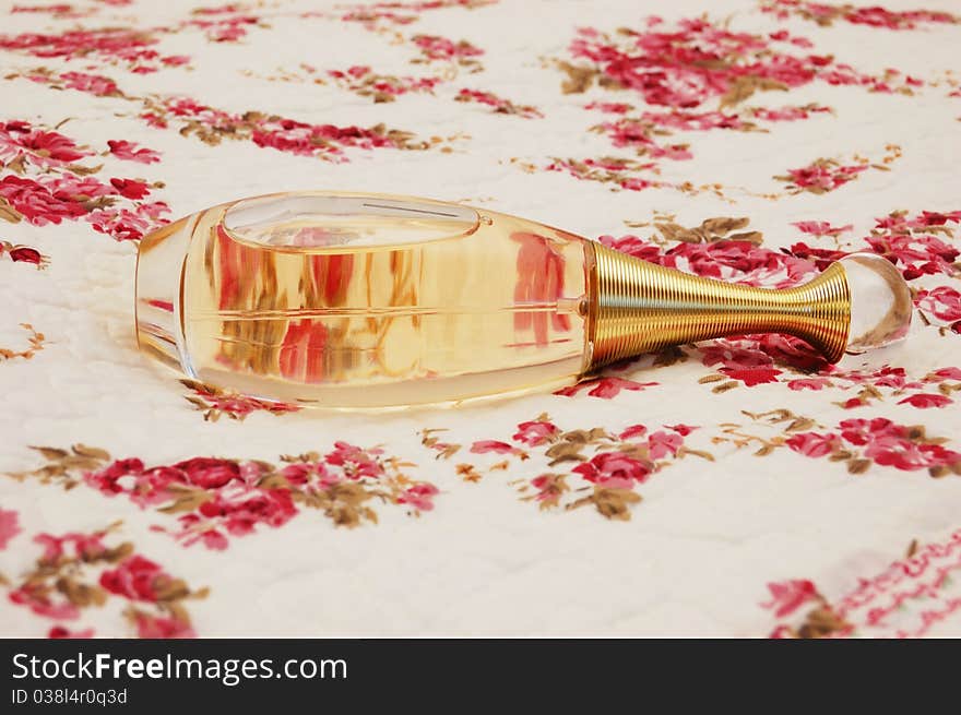 Bottle of perfume on white cloth with pattern of flowers. Bottle of perfume on white cloth with pattern of flowers