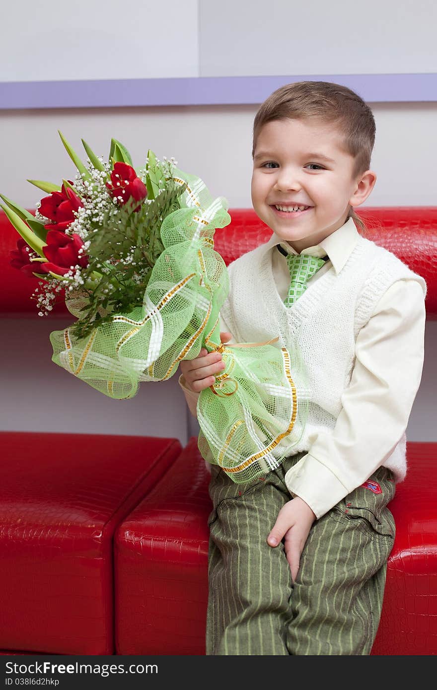 Little funny boy with flowers sitting on the couch