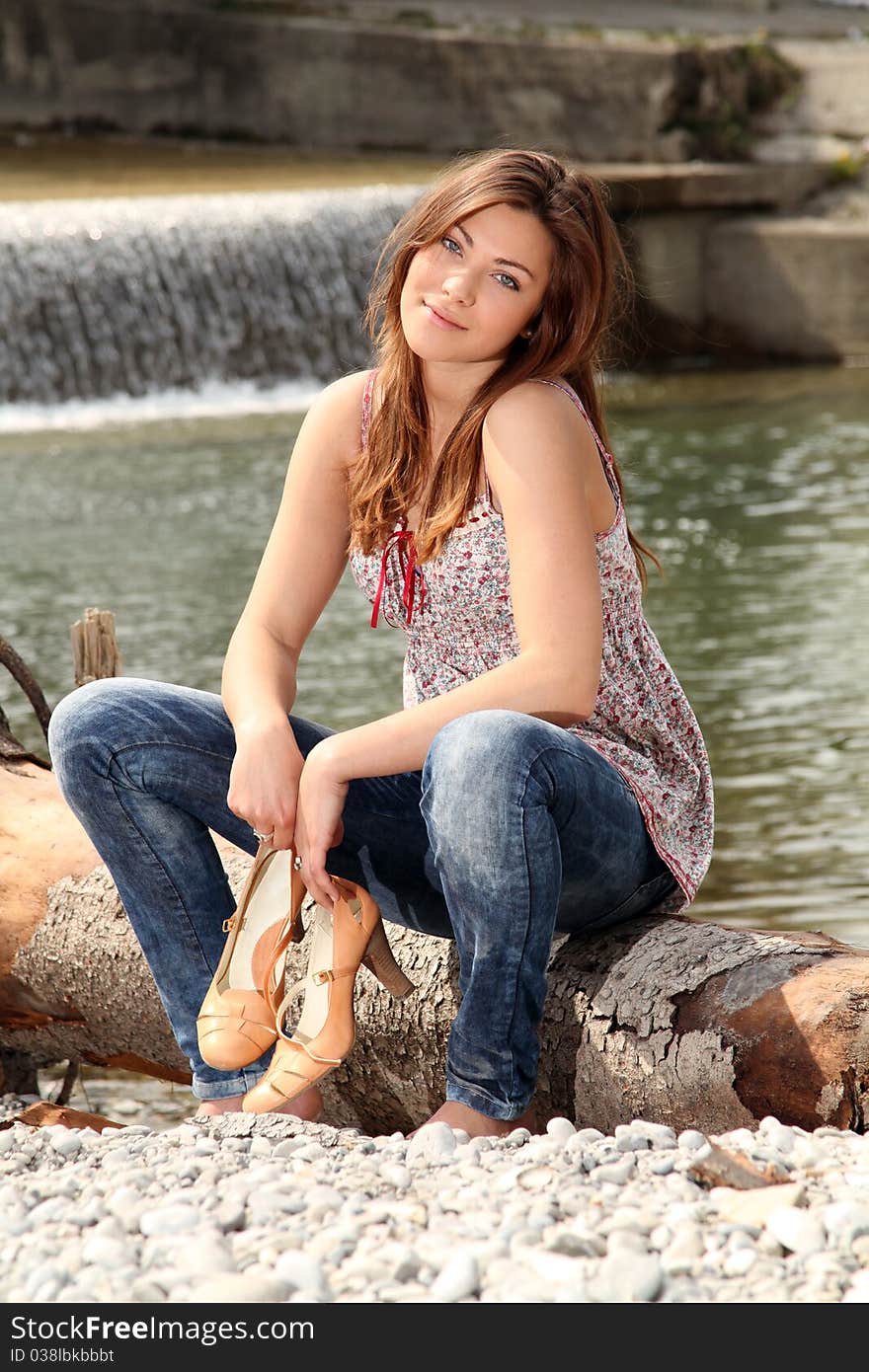 Young brunette woman sitting barefoot outside at a river