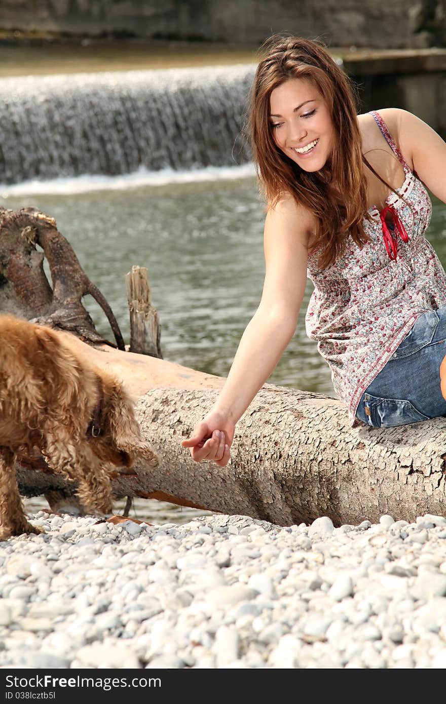 Young brunette woman sitting outside at a river playing with her dog. Young brunette woman sitting outside at a river playing with her dog