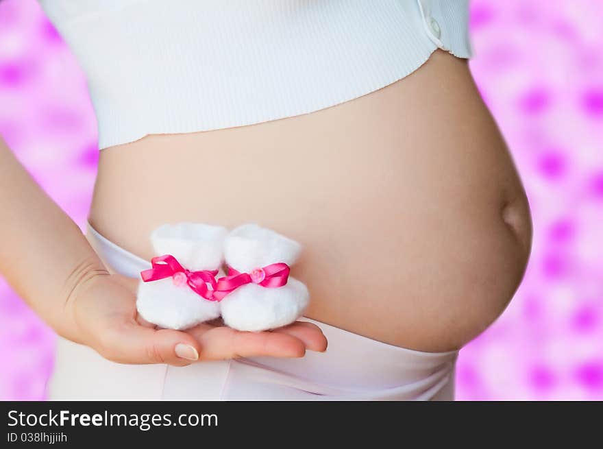 A pregnant woman holding baby shoes