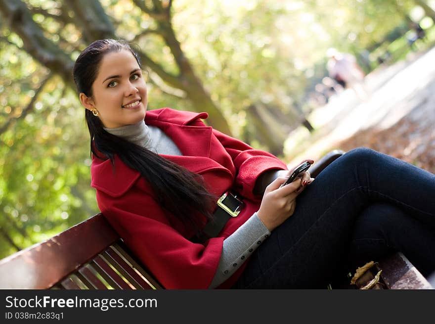 Young Caucasian woman with a cell phone, sitting in a park on a wooden bench, reading a SMS. Young Caucasian woman with a cell phone, sitting in a park on a wooden bench, reading a SMS.