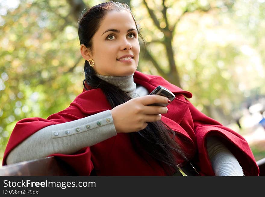 Young Caucasian woman with a cell phone, sitting in a park on a wooden bench, reading a SMS.