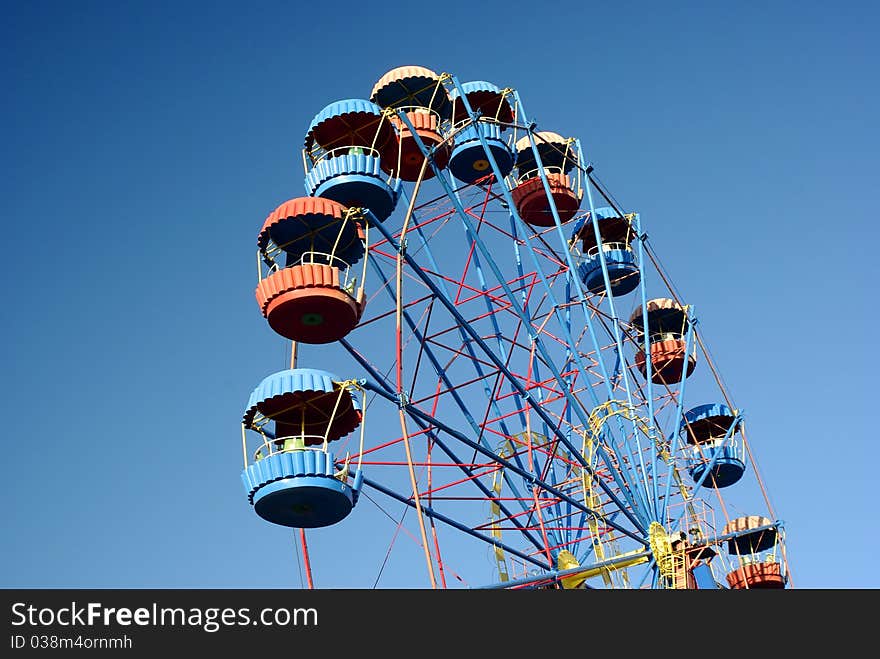 Low angle view of ferris wheel with colorful gondolas and blue sky background. Low angle view of ferris wheel with colorful gondolas and blue sky background.