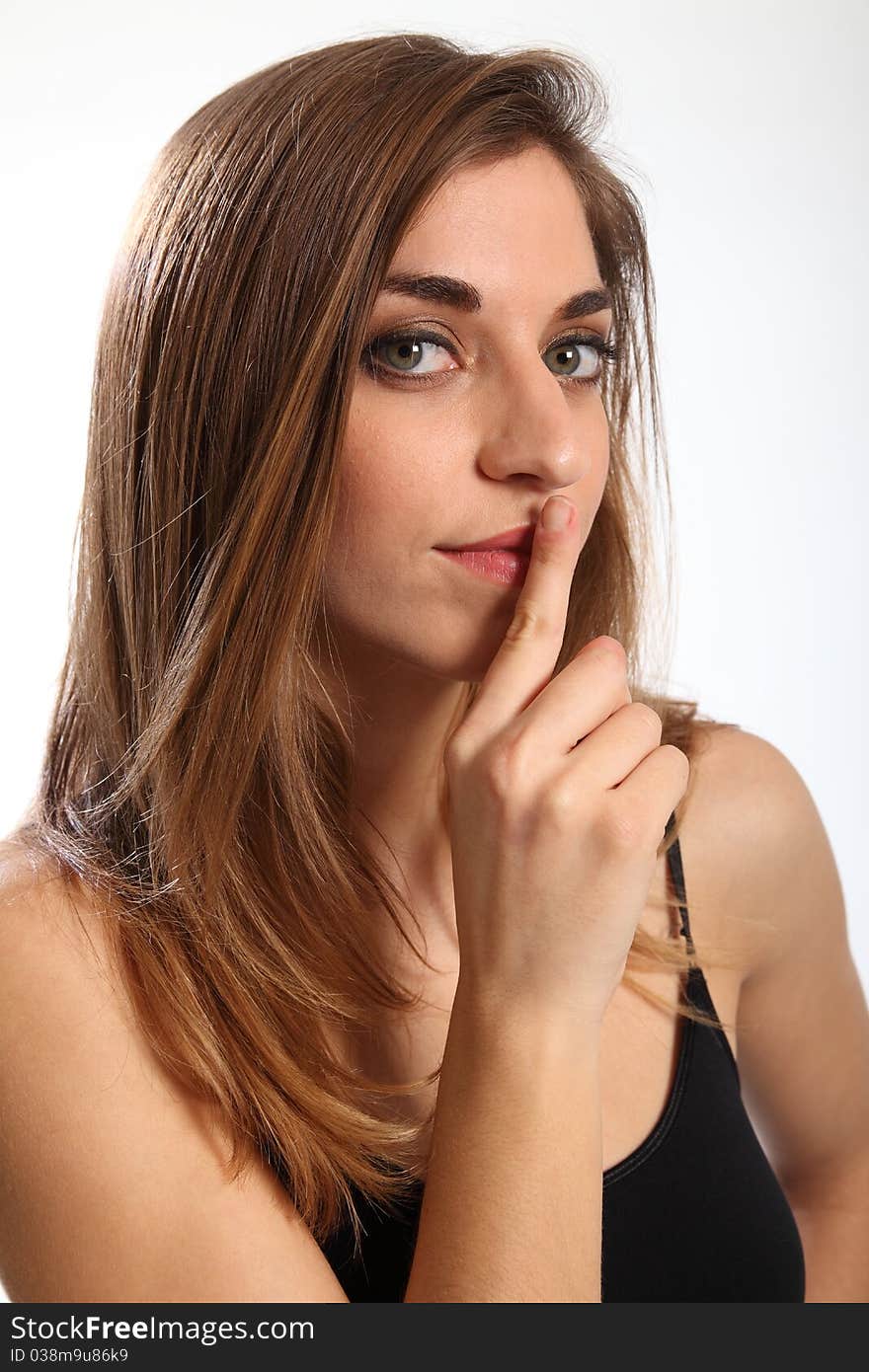 Headshot of beautiful young woman, finger over her lips, indicating quiet, or keep it secret. Model has serious expression on her face looking straight to camera. Headshot of beautiful young woman, finger over her lips, indicating quiet, or keep it secret. Model has serious expression on her face looking straight to camera.