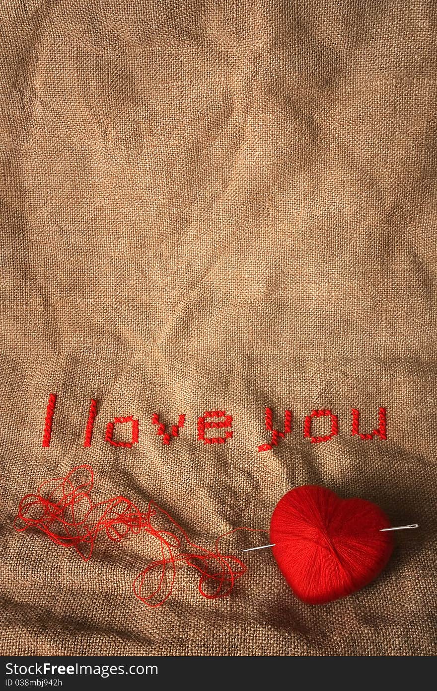 Cross stich 'I love you' with knit ball in a form of a heart pierced with needle. Cross stich 'I love you' with knit ball in a form of a heart pierced with needle