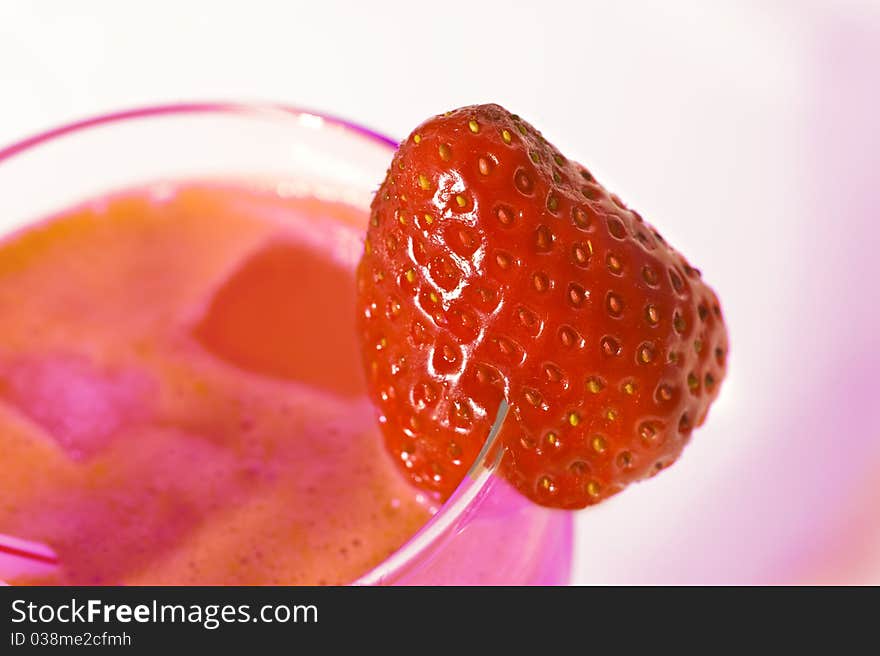 A fresh strawberry on the rim of a glass of multi colored juice. A fresh strawberry on the rim of a glass of multi colored juice