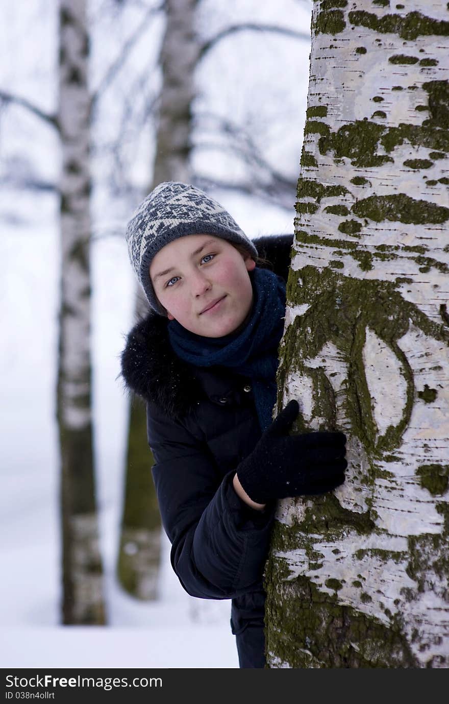 Young girl in winter hat looks out from the tree. Young girl in winter hat looks out from the tree