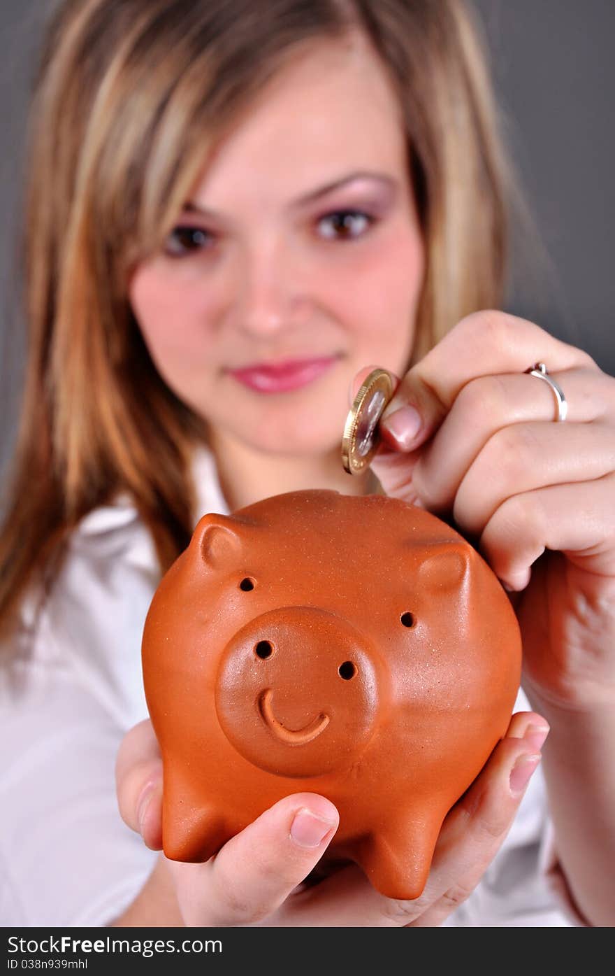 Beautiful young girl putting money in her piggy bank