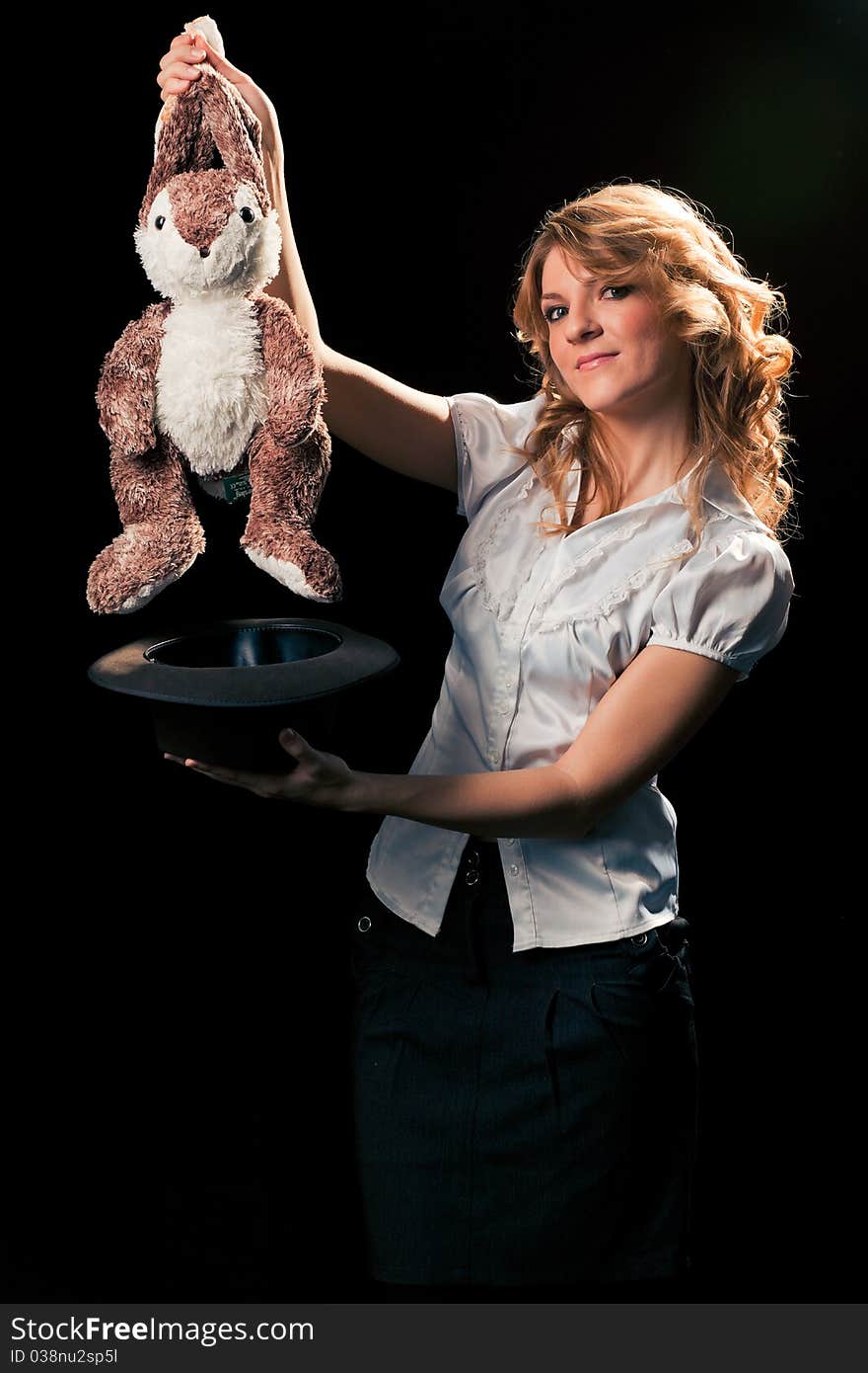 Pretty young grey-eyed blondie getting a toy rabbit out of the hat. Black background, ready for isolation. Pretty young grey-eyed blondie getting a toy rabbit out of the hat. Black background, ready for isolation