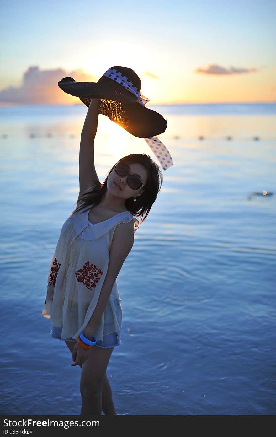 Girl on the beach of Saipan Island with the beautiful sunset.She put the straw hat in the air to cover the shining sun. Girl on the beach of Saipan Island with the beautiful sunset.She put the straw hat in the air to cover the shining sun.