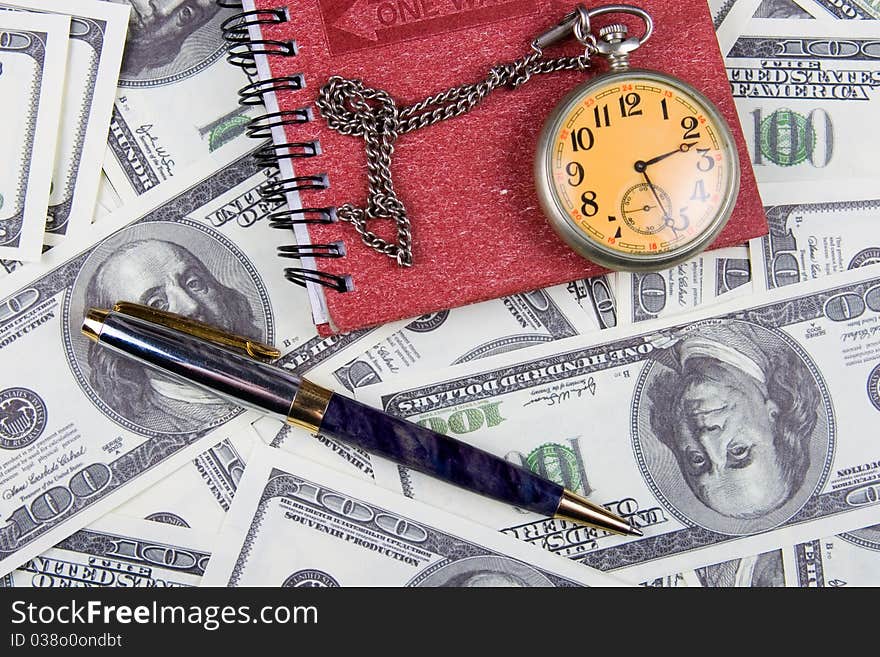 Pocket watch, notebook and pen on a stack of dollars, reflecting time and money