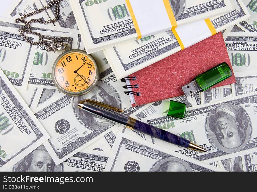 Pocket watch, notebook and pen on a stack of dollars, reflecting time and money