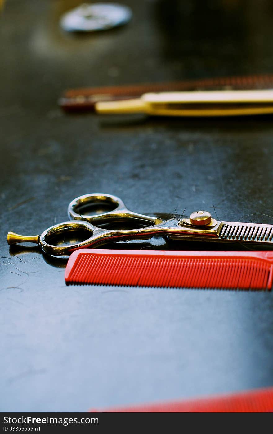 Barbers' thinning scissors with red comb on black work surface with white cut throat in background. Barbers' thinning scissors with red comb on black work surface with white cut throat in background