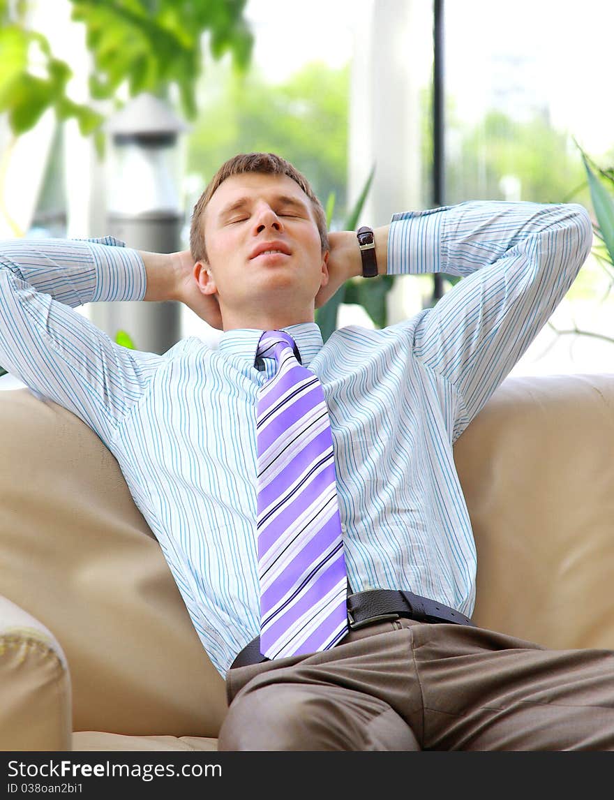 Young relaxed business man with hands behind head at work