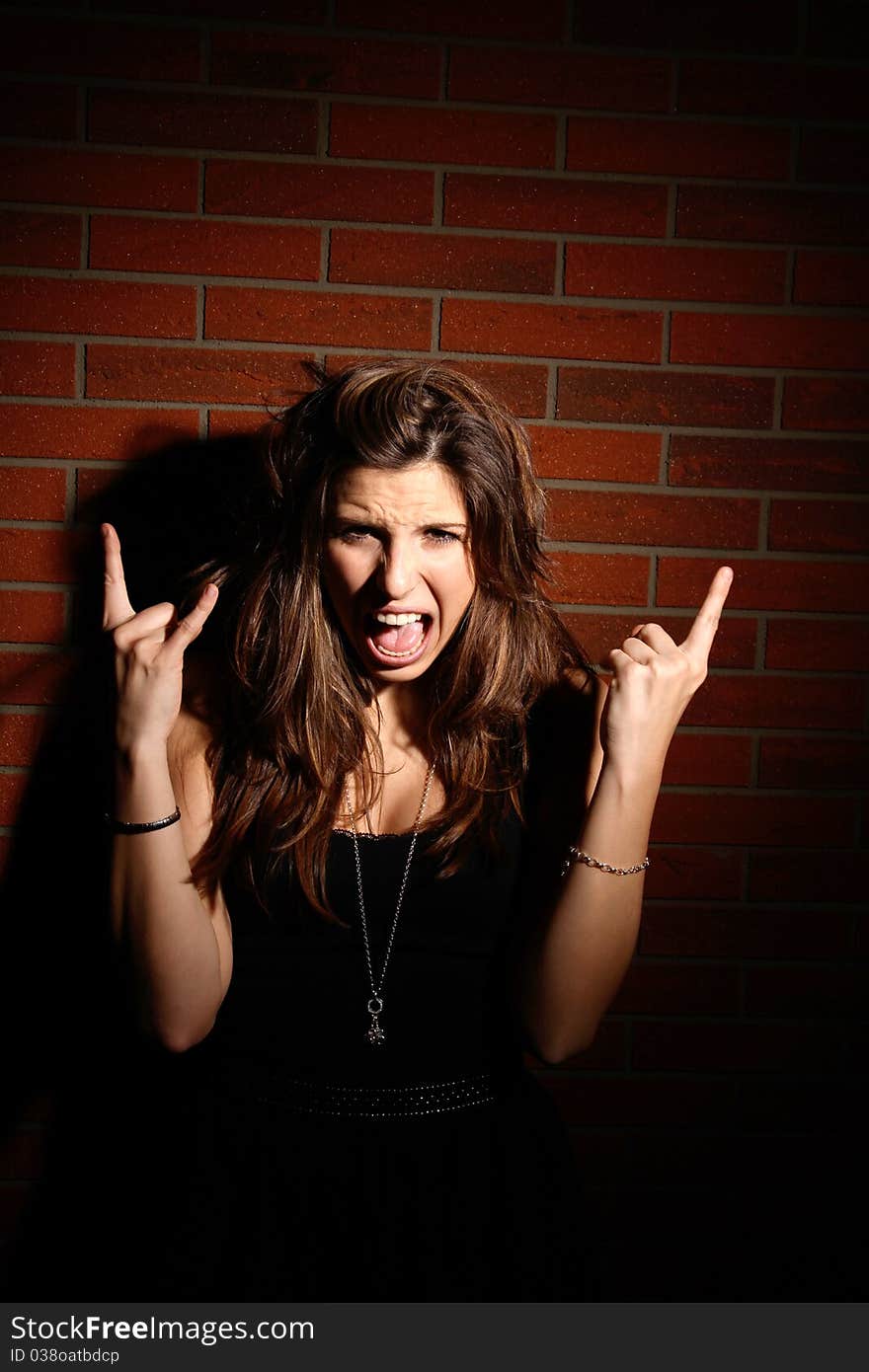 Beautiful young brunette girl giving a typical rock and roll hand sign. Beautiful young brunette girl giving a typical rock and roll hand sign