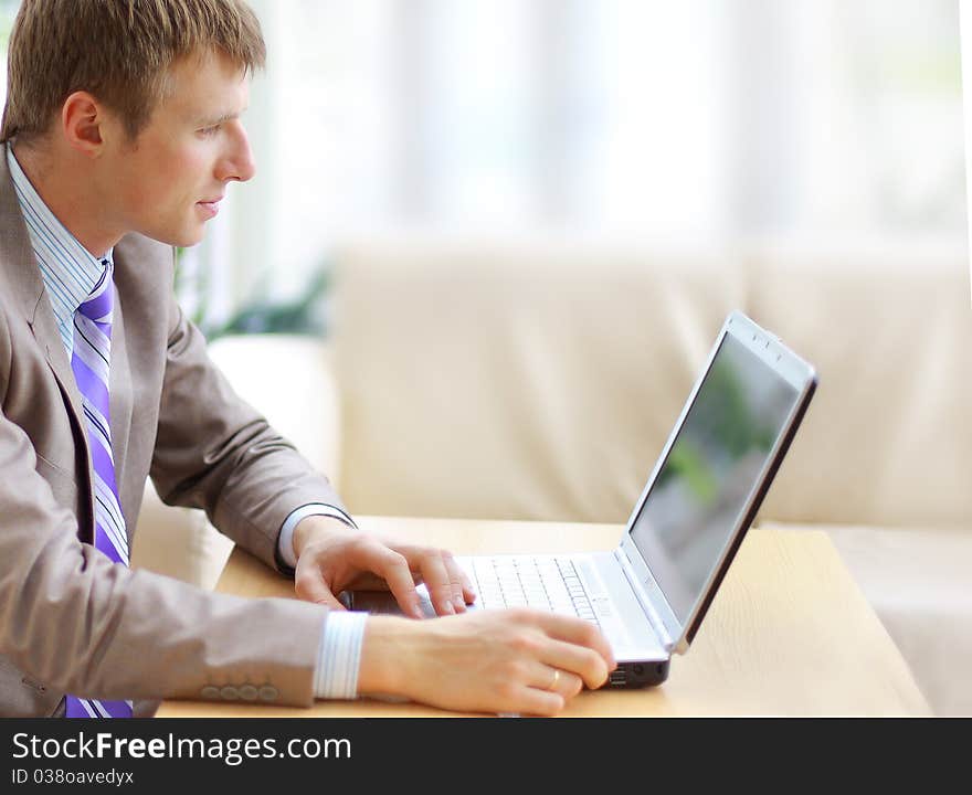 Businessman sitting at desk in office, working with laptop computer, looking back, smiling