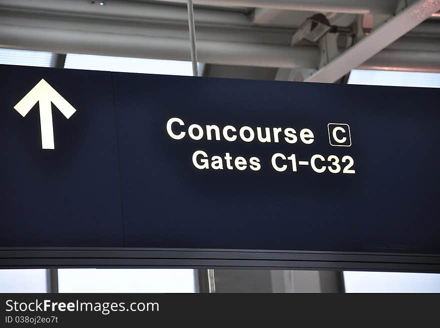 A dark blue airport sign reading Concourse C and Gates C1 to C32 in white with a directional arrow. A dark blue airport sign reading Concourse C and Gates C1 to C32 in white with a directional arrow