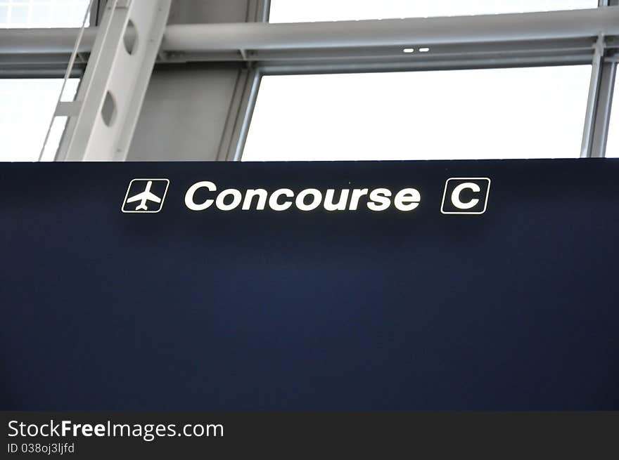 A dark blue airport sign reading Concourse C with a directional arrow in white. A dark blue airport sign reading Concourse C with a directional arrow in white