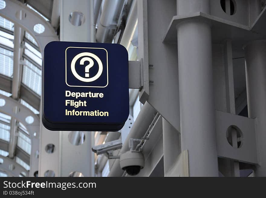 A dark blue sign reading Departure Flight Information with a question mark symbol against a gray industrial background