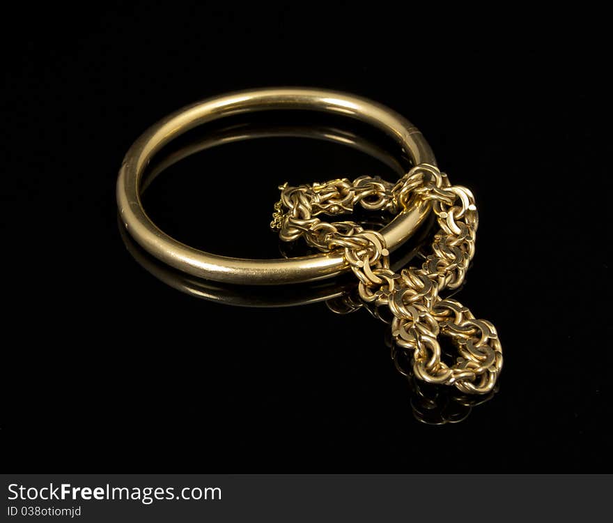 Close-up of two gold bracelets with reflex on black background