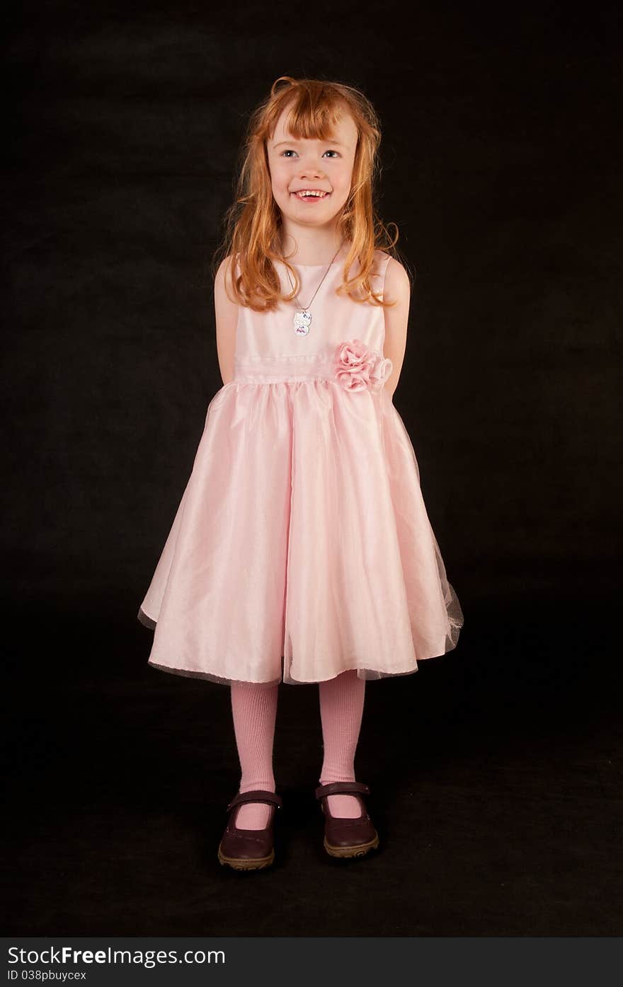 Cute little girl in pink dress against black background