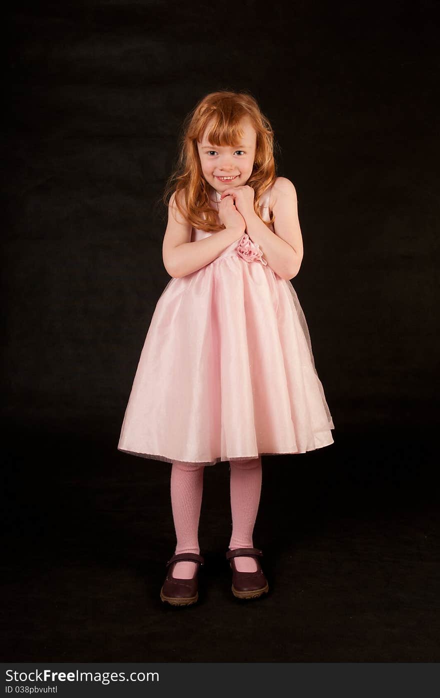 Cute little girl in pink dress against black background