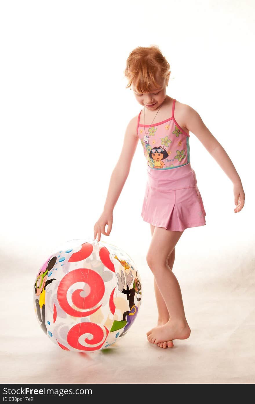 Cute little girl in pink swimsuit playing with a beach ball