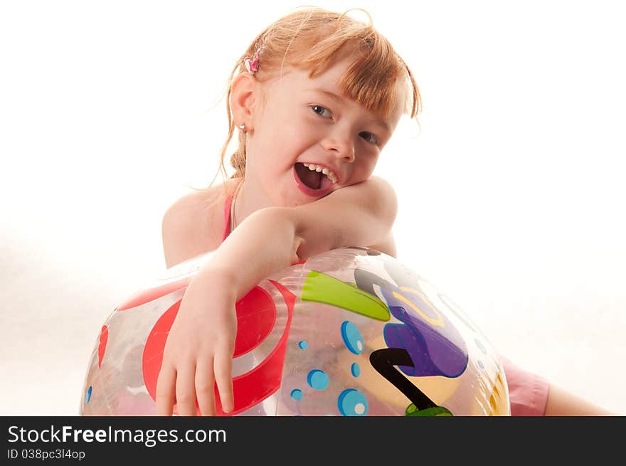 Cute little girl in pink swimsuit playing with a beach ball