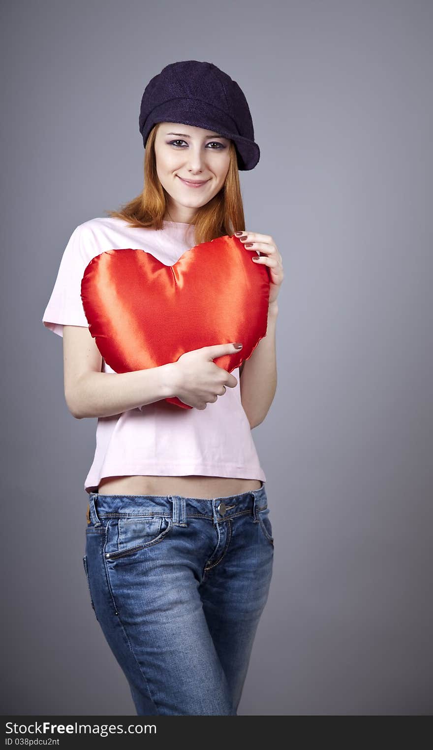 Beautiful red-haired girl in cap with toy heart. Studio shot.