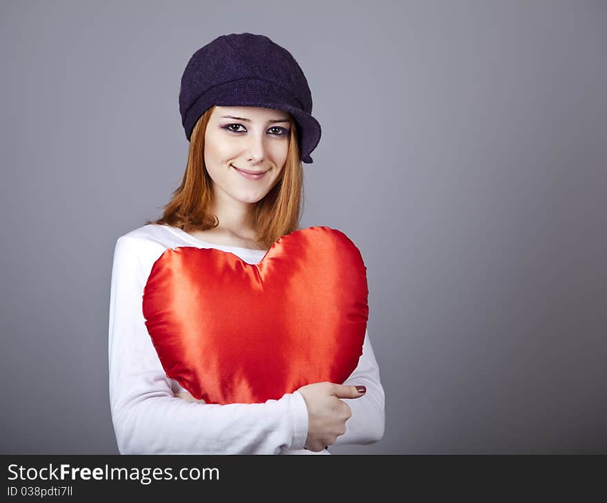 Beautiful red-haired girl in cap with toy heart.