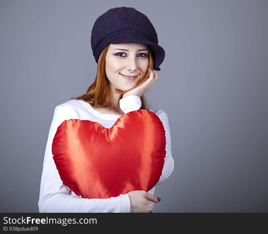 Beautiful red-haired girl in cap with toy heart. Studio shot.