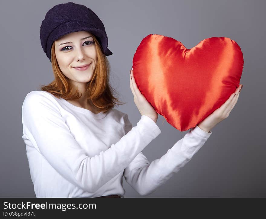 Beautiful red-haired girl in cap with toy heart. Studio shot.